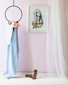 Damensandalen auf weisser Ablage neben kreisförmigem Metallgestell mit Tuch, von der Decke abgehängt, an rosa Wand gerahmtes Frauenportrait, seitlich luftiger Vorhang