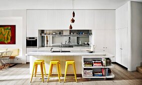White fitted kitchen with mirrored splash guard, kitchen island with marble worktop and yellow retro bar stools