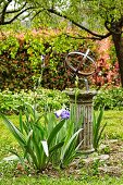 Blühende Iris vor alter Steinsäule mit Metall-Kunstobjekt in romantischem Garten