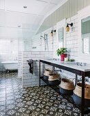 Spacious bathroom with black and white patterned floor tiles, modern washstand with marble top on black metal frame next to shower area and free-standing bathtub below window