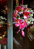 Wreath in various shades of red and pink hanging on glass door with brass fittings