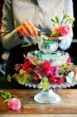 Hands of woman creating flower arrangement with roses on crystal fruit stand