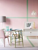 Verschiedene Stühle in Pastelltönen um Tulip Table, im Hintergrund weisser Sideboard vor rosa Wand mit grünen Streifen