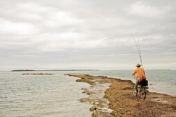 Man Riding Bicycle With Fishing Rods on Beach, Florida Keys, USA