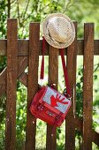 Strohhut & Umängetasche mit appliziertem rotem Hirschmotiv an Holzzaun hängend