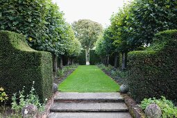 Balls on low walls either side of stone steps leading to lawn lined with trees