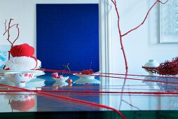 Oriental table setting: red woollen yarn wrapped around glass table, bowls, glass noodles on stacked plates and ball of red yarn