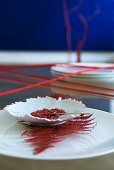 Oriental arrangement of red pepper in leaf-shaped dish on red fern leaf and white plate on table strung across with red woollen yarn
