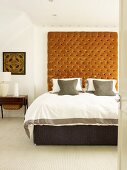 View through open door of double bed against wall with large, light brown upholstered panel