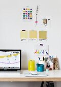 Laptop neben Kerzen auf Schreibtisch und Farbmuster an Wand; Moodboard