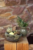Artichokes in hand-crocheted felt basket on wooden stool against stone wall