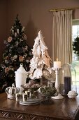 Weihnachtliches Stillleben auf Tisch - Schale mit Tannenzapfen zwischen brennender Kerze und weißem Glasbehälter vor geschmücktem Tannenbaum in Zimmerecke