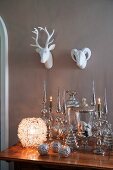 Spherical lantern next to silver Christmas decorations on antique table below china animal heads on wall