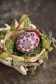 Egg artistically painted with white lace pattern in nest of twigs and moss decorated with shells