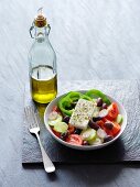 A Greek salad next to a bottle of olive oil