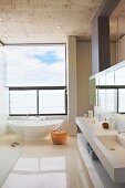 Geräumiges Designerbad mit freistehender weißer Wanne vor Panoramafenster, Doppelwaschbecken und Spiegel-Hängeschrankelement