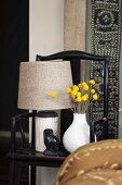 Still-life arrangement of table lamp, own ornament, antique Chinese wooden chair and ethnic wall hanging