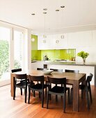 Solid wooden dining table in front of white designer kitchen with lime green splashback and access to terrace