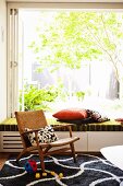 Gemütlicher Retro-Holzsessel auf grafischem schwarz-weißem Teppichmuster und geöffneter Fensterfront, Blick in den grünen sonnigen Garten