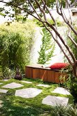 Gemütlicher Rückzugsort im sommerlichen Garten mit Holzsitzbank und rotem Polsterkissen