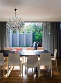 Spherical Dandelion lamp by Richard Hutten above dining table, pale plastic designer chairs and view onto terrace with blue-grey screen