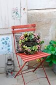 Autumnal wreath of vines, hydrangea flowers and acorns on garden chair with studded cushions; old door with nostalgic botanical prints in background