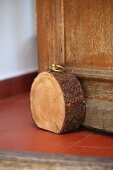 Rustic doorstop made from slice of tree trunk with straightened bottom edge and brass ring screwed into top