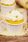 A cupcake decorated with buttercream and golden pearls