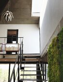 Black steel interior staircase and gallery with pendant lamp in natural form; green wall watered with rainwater in foreground