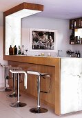 Designer bar stools at wood-clad counter and Corian worksurface in open-plan kitchen