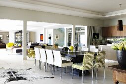 Chairs with patterned upholstery at long dining table in white tiled floor and lounge area behind pillars in open-plan interior