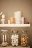 Reels of thread and storage jars on white shelves on sand-coloured wall