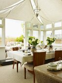 Gedeckter Tisch unter weissen Sonnensegeln an Decke im eleganten Wintergarten mit geöffneter Terrassentür
