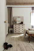 Antike Kleiderbank und Spiegelkommode in weißem Vintage Schlafzimmer; Dackelfigur als Türhalter auf dem Dielenboden