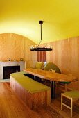 Gelbgrün getünchte Tonnendecke in Raum mit Esstafel und gebogener Sitzbank aus Holz vor modernem offenem Kamin