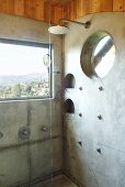 Dusche vor Fenster mit Ausblick in Badezimmerecke mit teilweise betonierter Wand und eingelassenen runden Ablagen