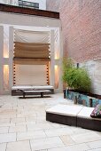 Modern, wicker sun loungers with pale cushions on stone-flagged floor of courtyard with awnings