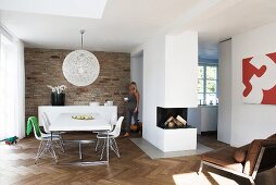 Open-plan interior with dining area, free-standing fireplace block and herringbone parquet floor; exposed brick wall behind dining area