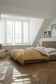 Sunny bedroom in natural shades with double bed in front of generous dormer window with interior, folding shutters