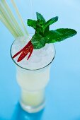 A cocktail garnished with lemongrass, mint and a chilli pepper