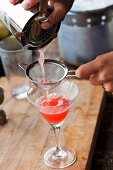 A cocktail being poured into a glass through a sieve