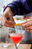 A cocktail being garnished with lemon zest