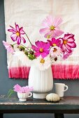 Blumenstrauss mit verschiedenfarbigen Cosmeen auf rustikalem Schemel, vor Dipped-Dyed-Tuch an Wand