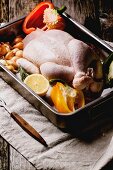 Raw chicken with vegetables in a roasting tin on old wooden table