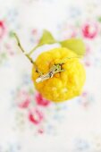 A lemon with a stem and leaves against an out-of-focus floral tablecloth