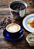 A cappuccino, coffee beans, sugar and a croissant