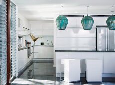 Modern white open-plan kitchen; bulbous metal pendant lamps above counter with white designer cubic bar stools