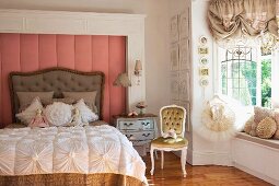 Romantic scatter cushions and ornate bedspread on antique bed against wall panel with dusky pink cover next to tutu on clothes hanger in bay window with ruched curtains
