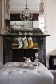 Fireplace decorated with Christmas stocking, garlands and glass reindeer below elegant mirror; silver tray on ottoman in foreground