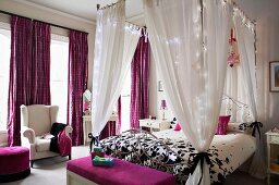 Elegantes Schlafzimmer mit beleuchtetem Himmelbett und Textilien in Lila